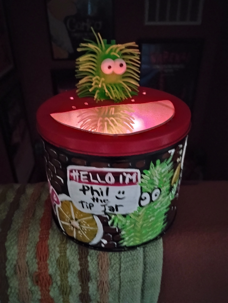 Phil the Tip Jar featuring a glowing red interior, a green shaggy creature topper, and a hand-painted name tag.